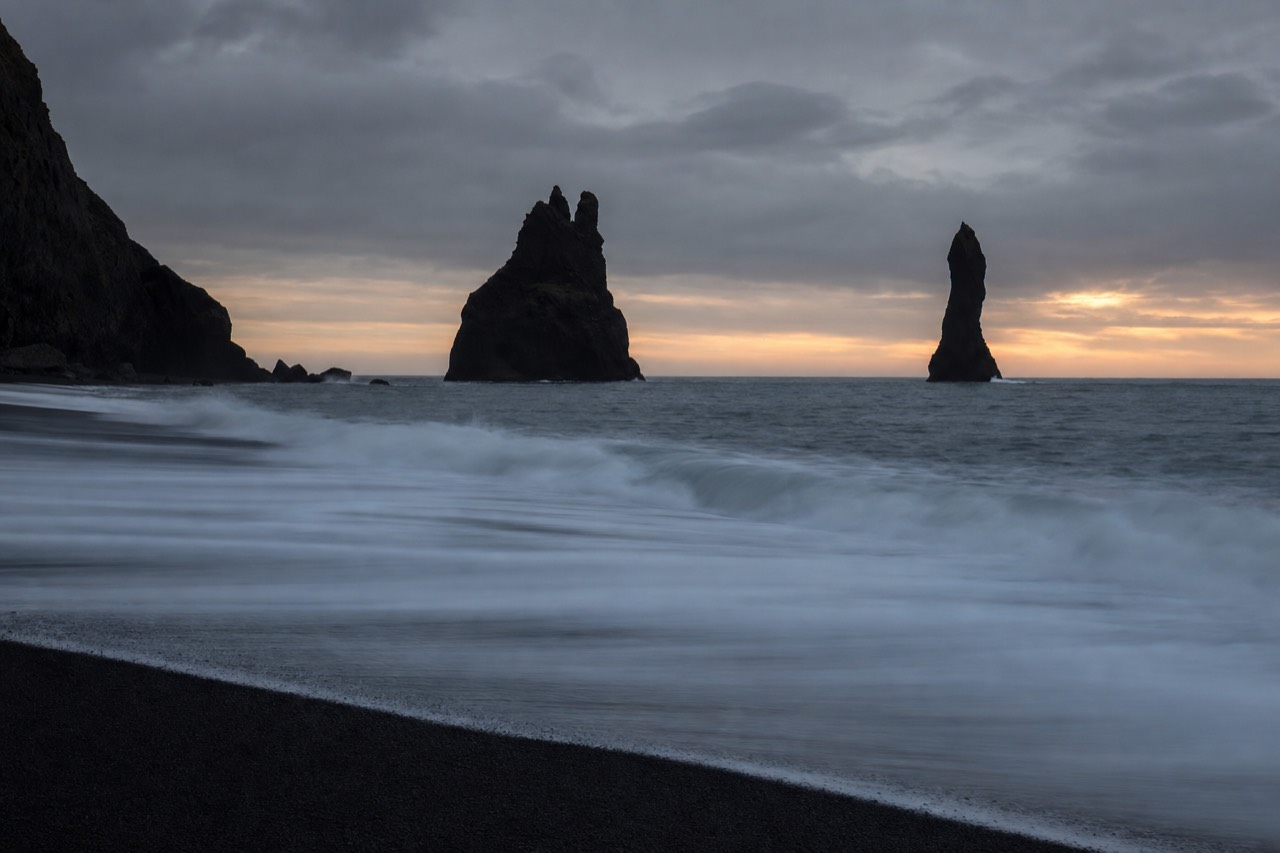 The Reynisdrangar sea stacks silhouetted against a low dusk sky off the black sand of Reynisfjara