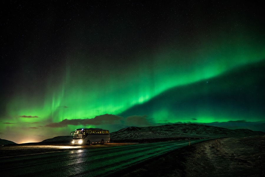 The aurora borealis glowing green over a dark rural road near Reykjavik on a northern lights bus tour